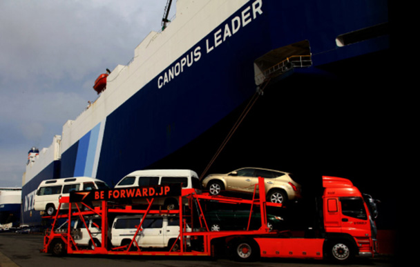 BE FORWARD car carrier truck loading vehicles onto a large cargo ship at the port for international export.